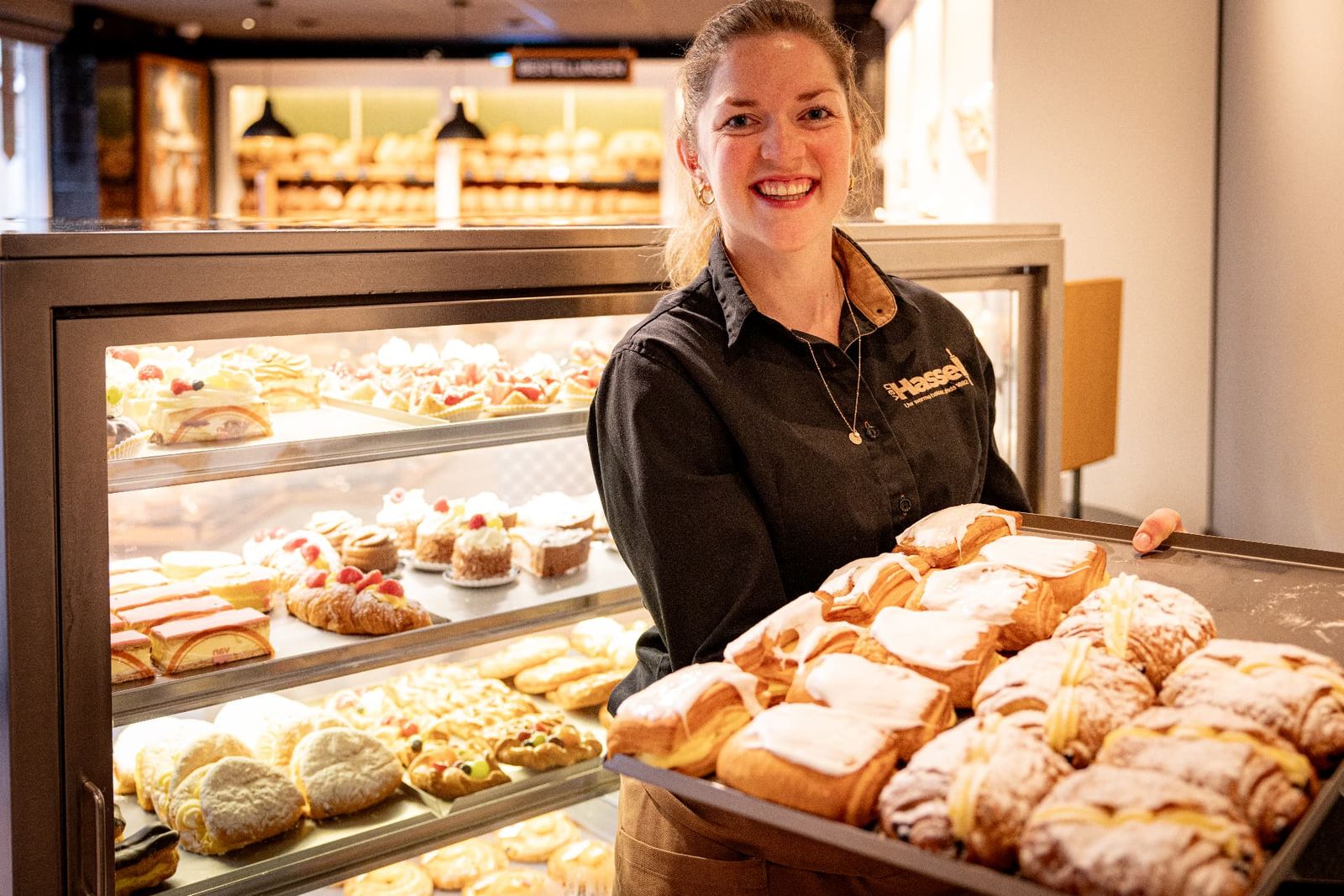 Medewerkster van Bakkerij van Hassel met een plateau vers gebak in de winkel