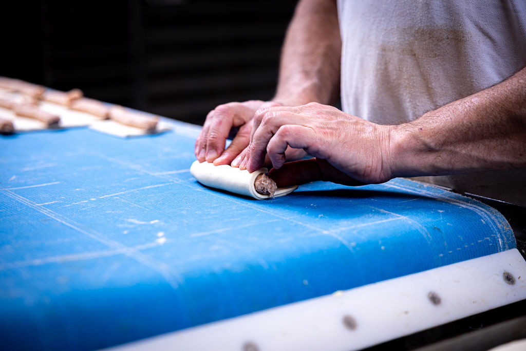 Bakker rolt met de hand een worstje in het deeg bij Bakkerij van Hassel